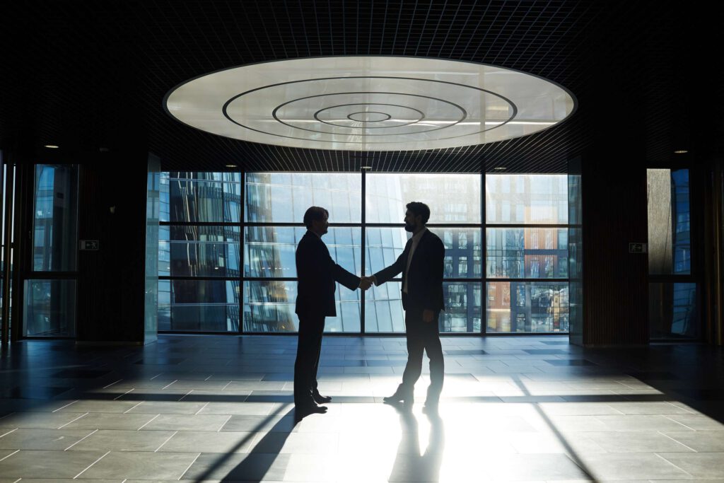 Two entrepreneurs handshaking in office center against window with sunlight penetrating inside