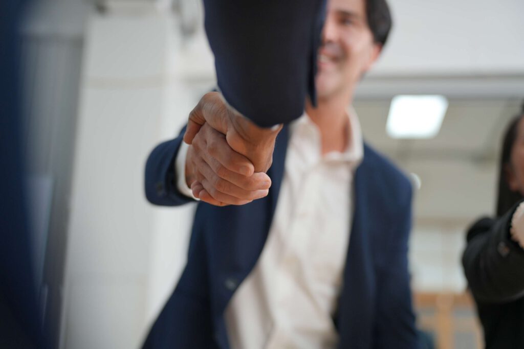 Geschaeftsleute geben sich zur Begrueßung die Hand, symbolisierend die Kombination von technischem Wissen und betriebswirtschaftlichen Loesungen im M&E-Ansatz.